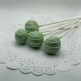 Three key lime green cake pops on white sticks, presented on a lace doily.